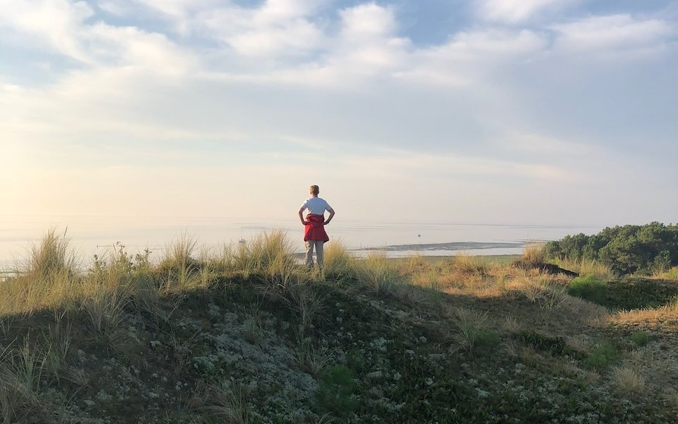 Een vrouw staat op een duintop en kijkt uit over de Waddenzee
